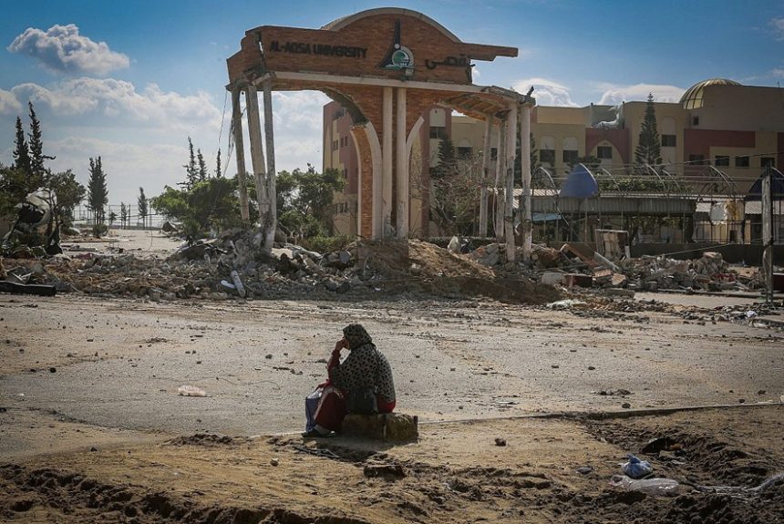 Una mujer palestina sentada frente a la entrada dañada de la Universidad Al-Aqsa en Khan Younis, al sur de la Franja de Gaza, el 26 de enero de 2024. (Atia Mohammed/Flash90)